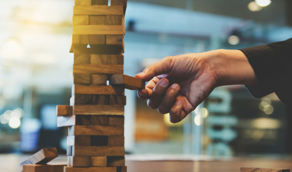 Hand removing a wooden block from a Jenga game, illustrating an article on pension risk