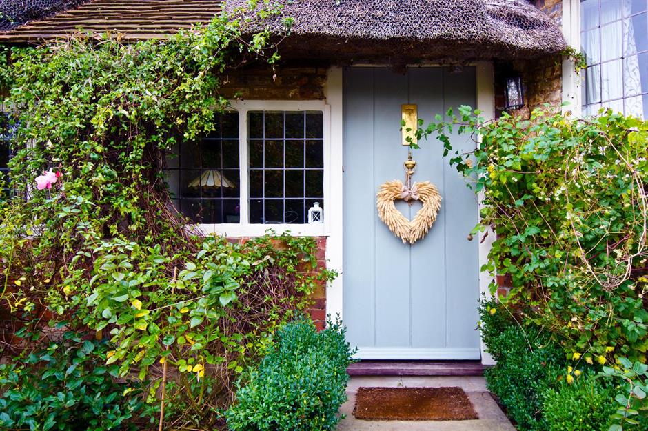 A photo of a blue front door of a cottage. The door is surrounded by vines and plants. A heart-shaped wreath hangs on the door. The photo is to illustrate equity release.