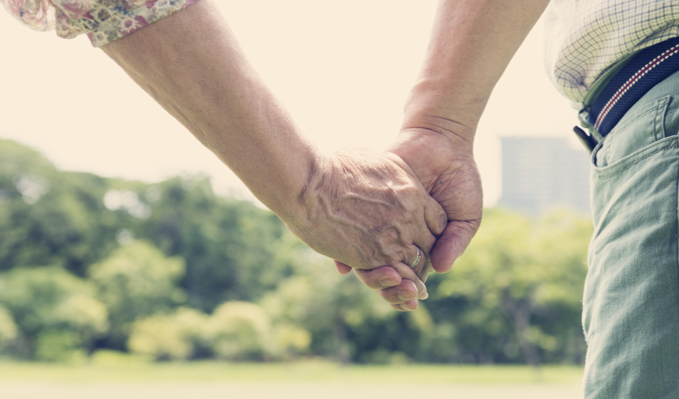 A close up of an older couple holding hands in a park, illustrating an article on improving financial security
