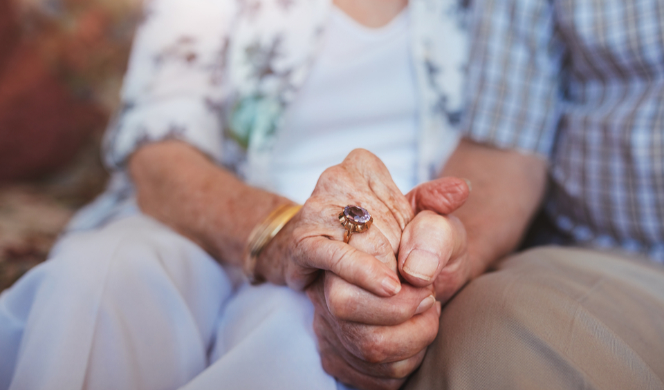 A close up of an elderly couple holding hands, illustrating an article on protecting vulnerable family members from financial abuse