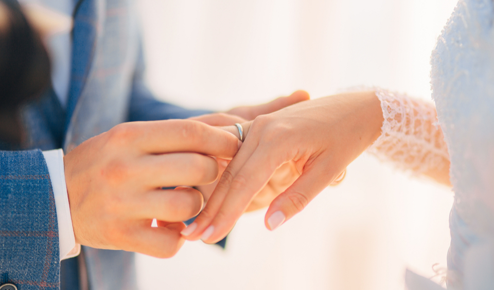 A couple exchanging wedding rings, illustrating an article about the financial reasons to get married