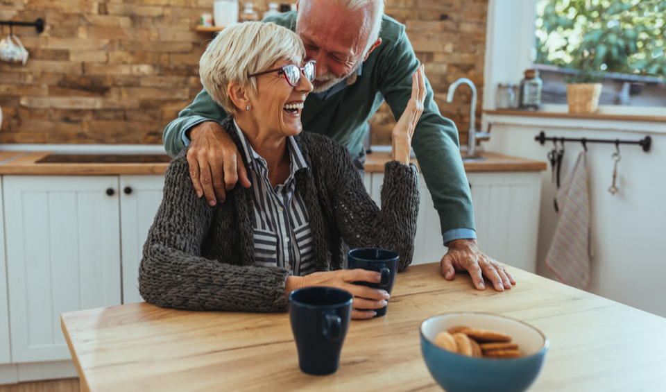 An older couple laughing together in their kitchen illustrating an article on estate planning